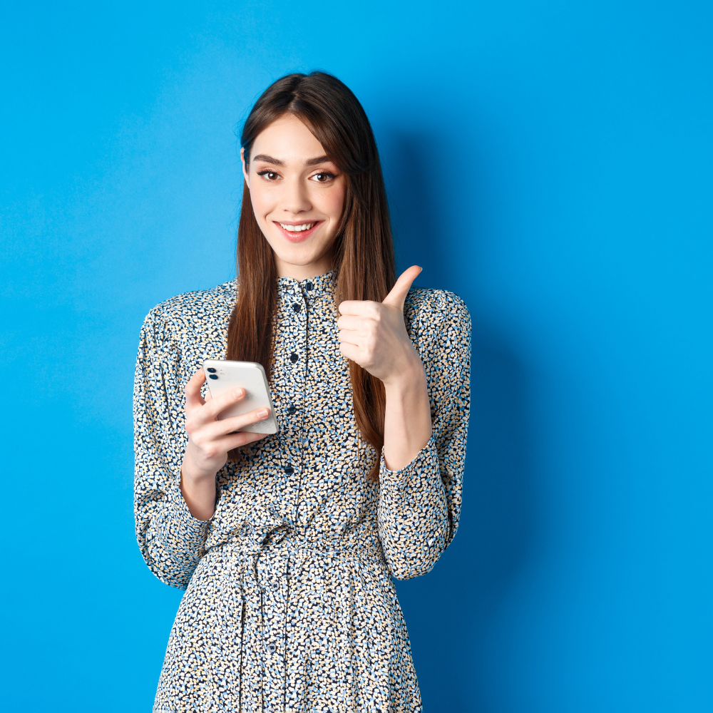 smilling woman holding a smartphone and giving a thumbs-up, representing career opportunites after completing an ai course