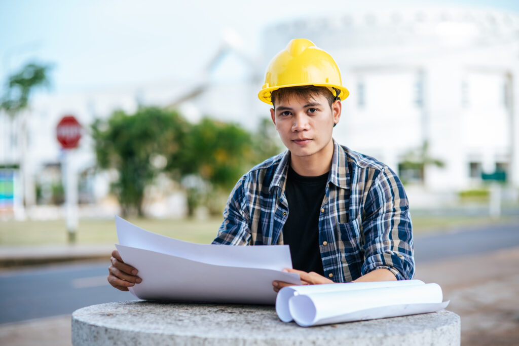 Engineering student wearing safety helmet reviewing construction blueprints